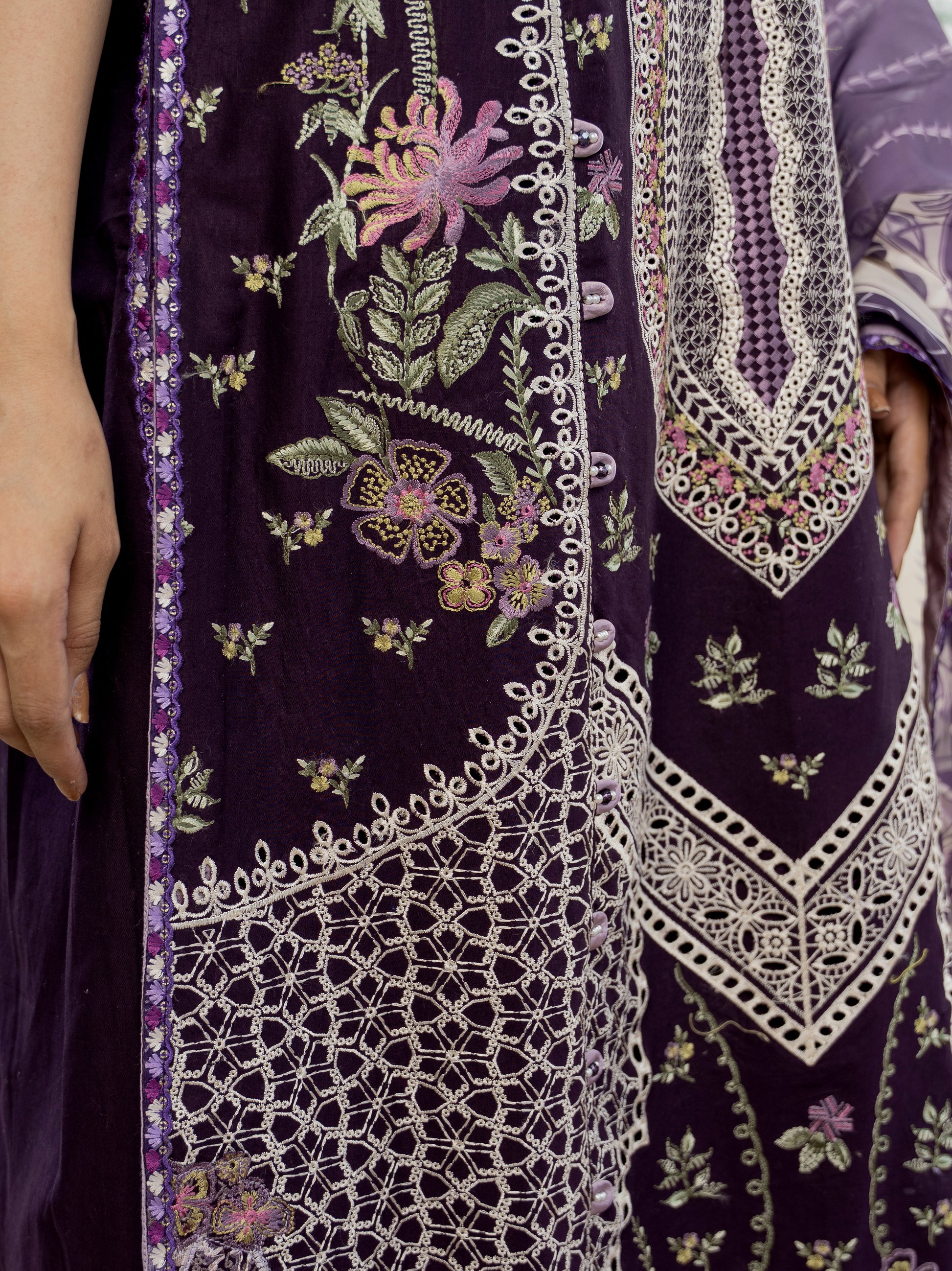 Close-up of a dark purple fabric with intricate white embroidery and floral patterns.