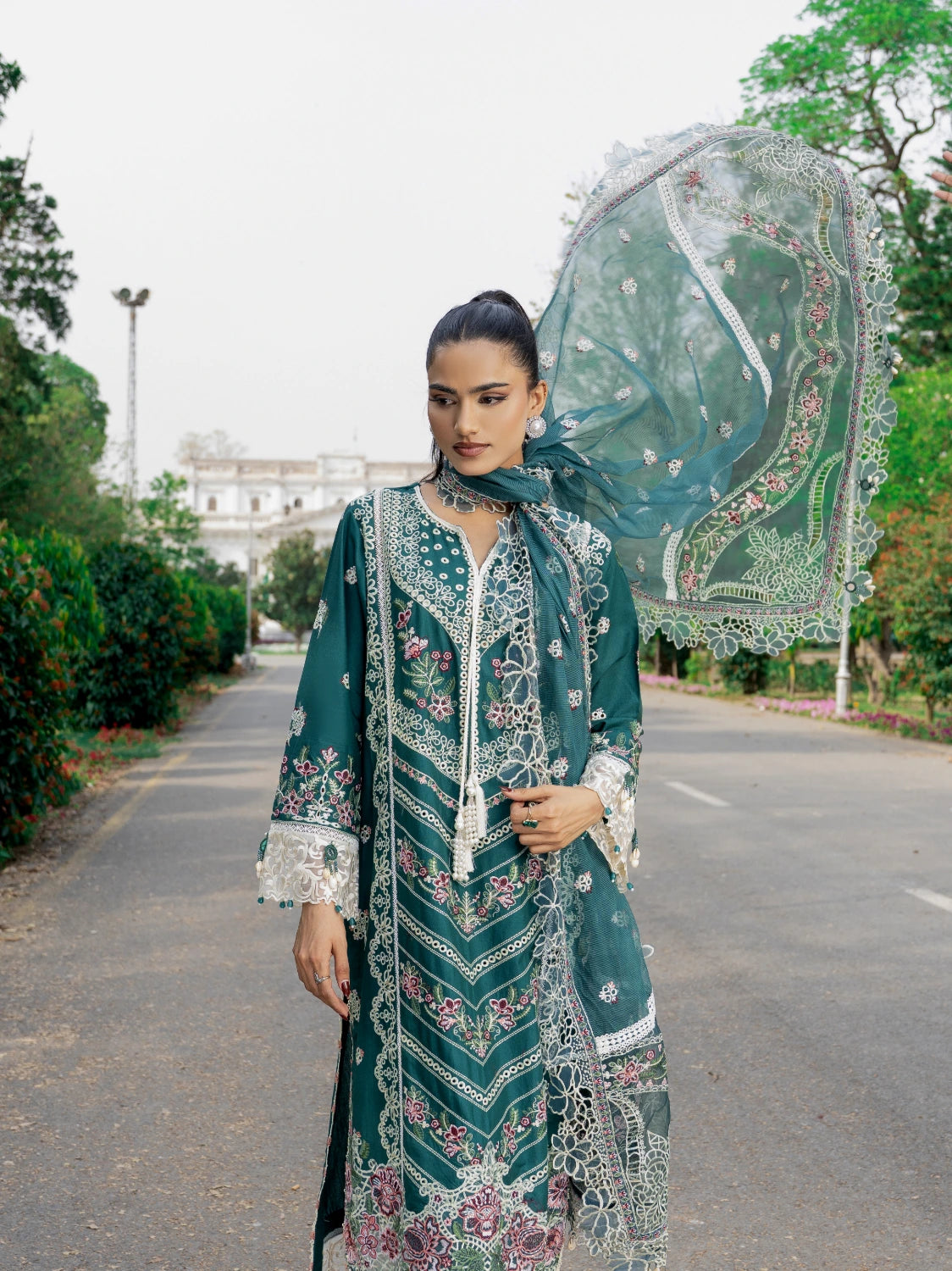 Woman in traditional green and white embroidered outfit holding a decorative parasol outdoors.