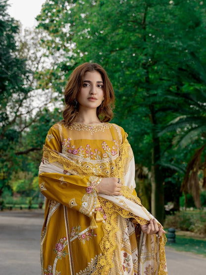 A woman wearing a traditional embroidered yellow and white salwar kameez suit with a matching dupatta, standing outdoors in a park with green trees in the background.