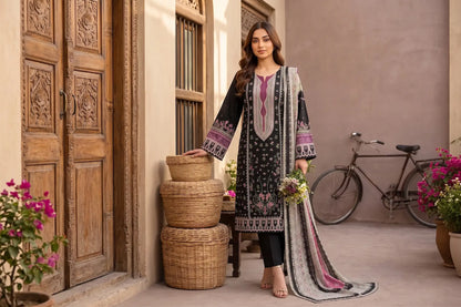 A woman models a black 3-piece salwar kameez suit with intricate purple and white embroidery, paired with black trousers and a matching patterned dupatta, set against a rustic courtyard backdrop with wooden doors, woven baskets, and a bicycle.