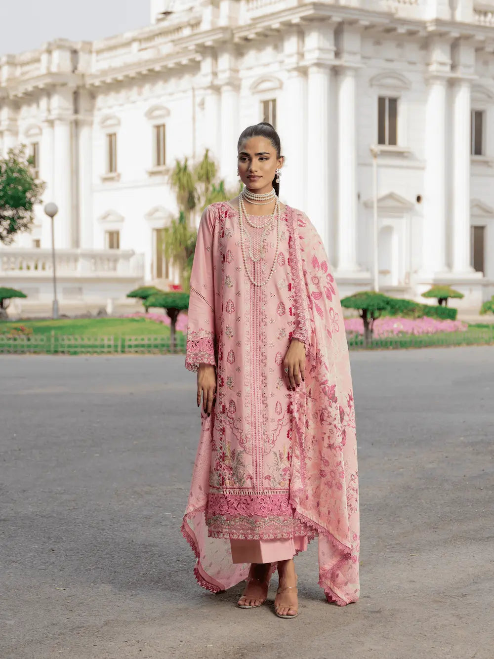 Woman in a pink traditional outfit standing in front of a large white building.