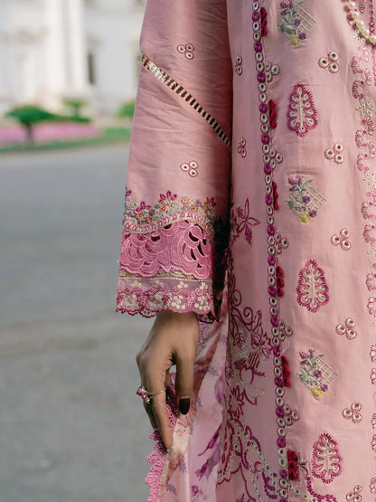 A close-up of a pink embroidered traditional garment with ornate floral and geometric embroidery, featuring a decorative scalloped sleeve cuff and a hand holding the fabric.